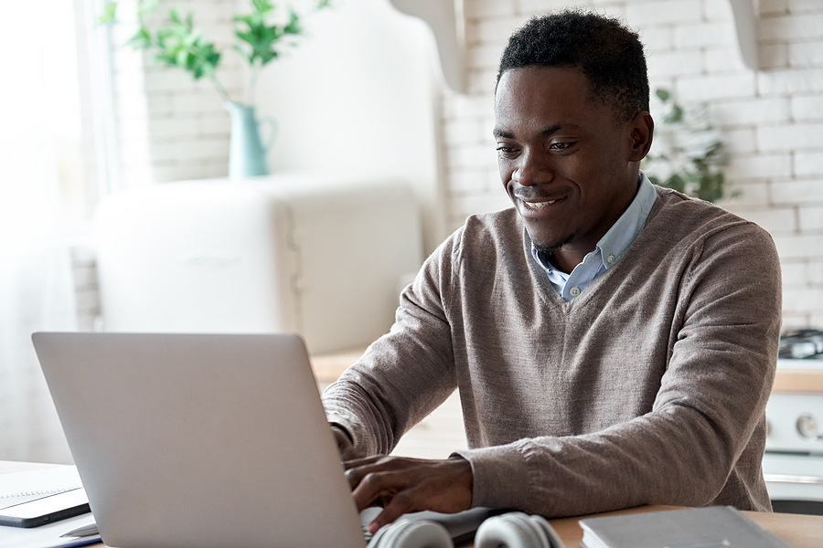 Smiling professional black business man using laptop computer working from home office.